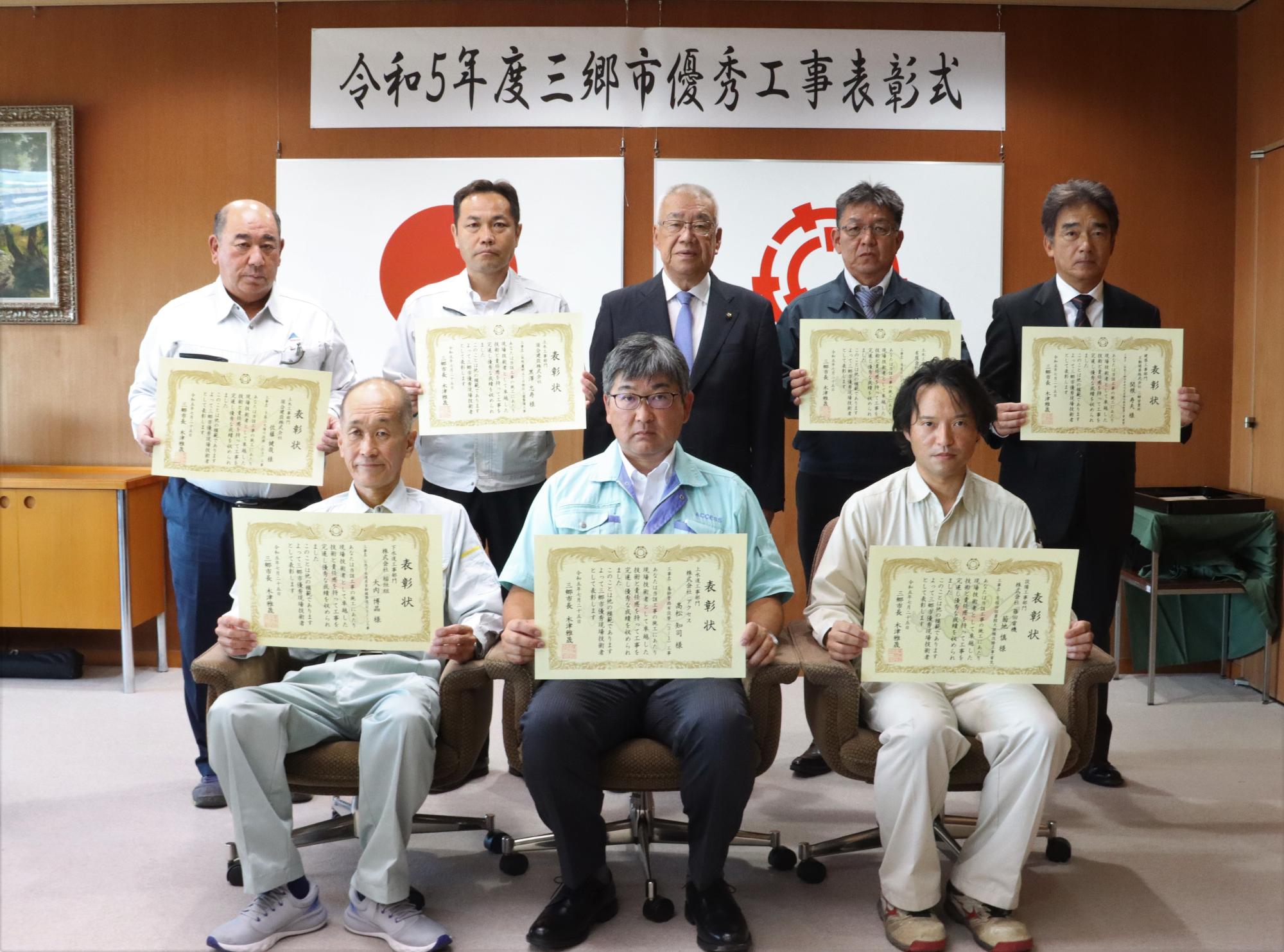 7名の男性が表彰状を持ち、木津市長とともに記念撮影をしている写真