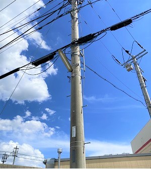青い空と白い雲をバックに、電柱に設置された防犯灯を下から写している写真