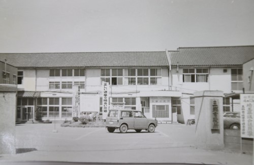 入り口の傍に設けられた駐車場に2台の車が駐車している2階建ての旧庁舎の白黒写真