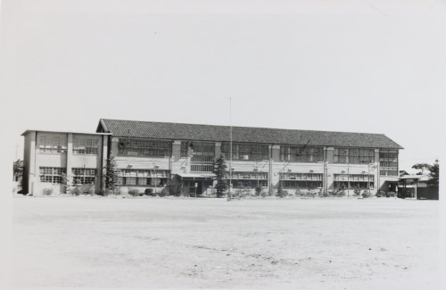 2階建ての小学校の校舎を運動場から撮影した白黒写真