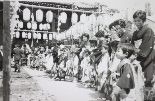 提灯が飾られたお寺の境内で和装姿の母親と袴を身に着けた子ども達が一列に並んでいる白黒写真