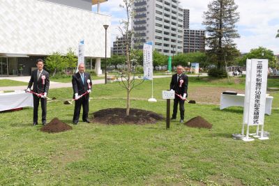 スーツを着た(左から)武居議長、木津市長、宅建協会 木村支部長がスコップを持ち、植樹したシイノキと一緒に記念撮影をしている写真