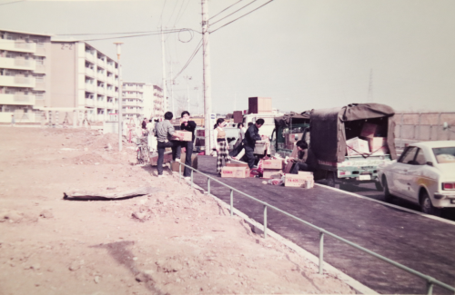 団地の手前の道路に停車した軽トラックから荷物を運び出している人達の写真