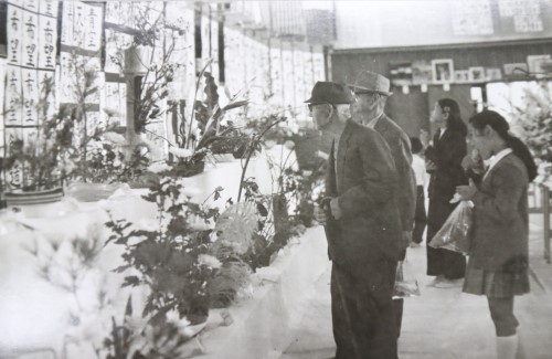 会場に展示された生け花や書道などの作品を鑑賞している方々の白黒写真