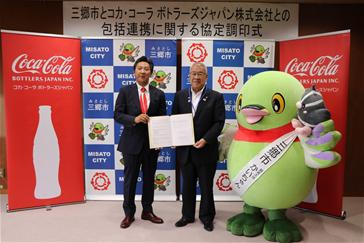 (左から)関東営業本部長 井上豊理事、木津市長、かいちゃんとつぶちゃんが横一列に並び、井上豊理事と木津市長が一緒に協定書を持って記念撮影をしている写真