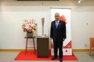 赤い絨毯の中央に設置された台の上にオリンピックの聖火リレートーチが置かれ、横に立って記念撮影をしているスーツ姿の木津市長の写真