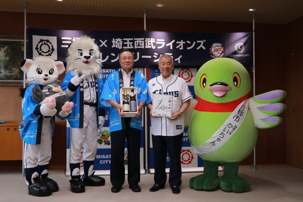 株式会社西武ライオンズのライナ、レオ、居郷社長、木津市長、かいちゃんが横一列に並び記念撮影をしている写真