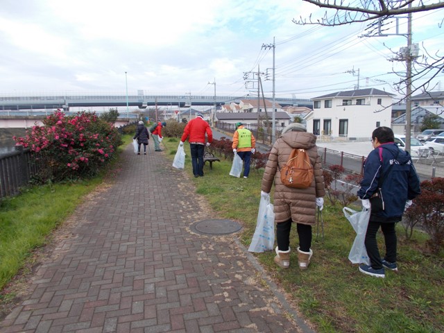 両側に芝生や植木がある歩道を歩き、ゴミ袋を持ちごみを回収している役員の方々の写真