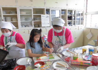 エプロン姿の女性が、参加者の女の子と一緒にまな板上の食材で作業をしている写真
