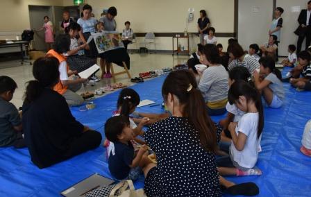 子供達と保護者の方々がブルーシートに座って作業をしている写真