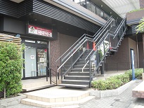 1階の自動ドア入り口に「にこにこ」の看板が設置され、2階へ続く外階段がある外観写真