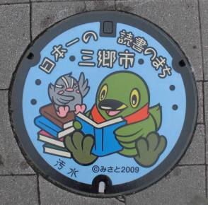 「日本一の読書のまち三郷市」の文字と、かいちゃんとつぶちゃんがなかよく本を読んでいる絵が描かれたマンホール蓋の写真