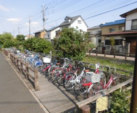 歩道の横に木造でつくられた駐車スペースがあり、たくさんの自転車が横一列で駐車され、奥に民家が建ち並んでいる大場川サイクルアンドバスライドの写真