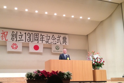 「祝創立130周年記念式典」と書かれた横断幕の下のステージの演壇で挨拶を行っている市長の写真