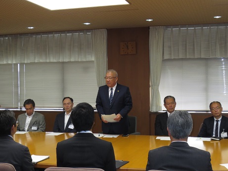 大きなテーブルの席に関係者が座り、中央の席から立ち上がり資料を持って話をしている市長の写真