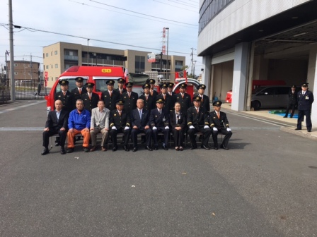 第5分団第1班のメンバーと地元町会長が赤い消防自動車の前に並び記念撮影をしている写真