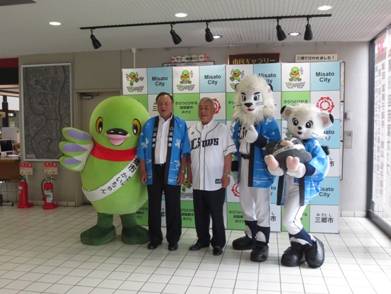 三郷市のバックボードの前で居郷社長、球団マスコットのレオ&ライナ、かいちゃんとともに記念撮影をしている市長の写真