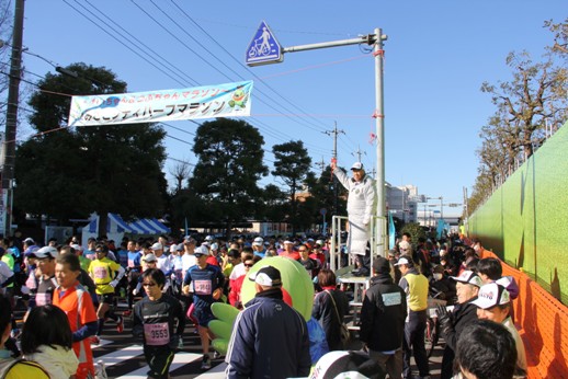 右手にピストルを持った市長の合図で大勢の参加者が走り始めたマラソン大会の様子の写真