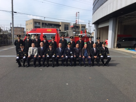 第2分団第4班のメンバーと地元町会長が赤い消防自動車の前に並び記念撮影をしている写真