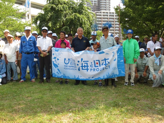 青を基調とした「海と日本」と書かれた横断幕を広げ、市長やたくさんの参加者たちが芝生上に並んでいる写真