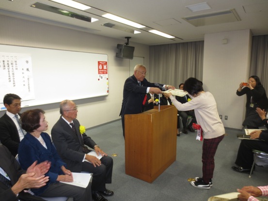 多くの関係者が座っている部屋で、市長と女性が向かい合って市長賞の贈呈が行われている写真