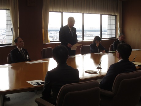 席を立ち資料を手に持って挨拶の言葉を述べる三郷市長と、座って話を聞くアルフレッサ株式会社様、株式会社スズケン様、東邦薬品 株式会社様、株式会社メディセオ様の社員と関係者の写真