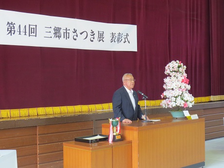 「第44回三郷市さつき展表彰式」と書かれた横断幕の下の演壇で挨拶を行っている市長の写真