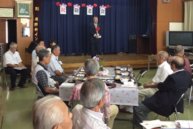 仁蔵会館の小さなステージの上で挨拶を行っている市長の話を着席して聞いている参加者の写真