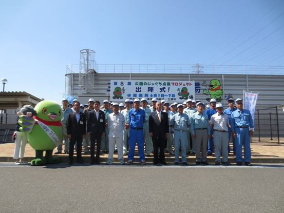 「公園のじゃぐち点検プロジェクト出陣式」と書かれた看板が下げられている屋外で、作業服を着た組合員とともに記念撮影をしている市長とかいちゃんの写真