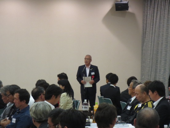 会場にたくさんの関係者が座っており、市長がマイク台の前に立って話をしている写真