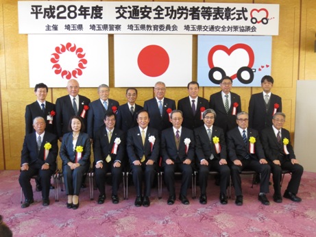 「平成28年度交通安全功労者等表彰式」の横断幕と埼玉県の旗、国旗などが掲げられた壁の前で、受賞者が前後2列に並んで正面を向いている記念写真