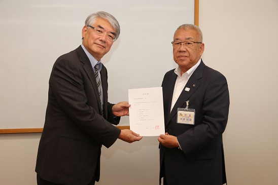三郷市長が男性とともに「第7期三郷市介護保険事業計画の策定」についての諮問書を手に持ち記念撮影をしている写真