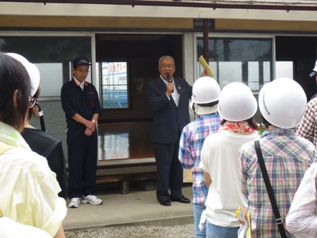 公民館の建物の前で、ヘルメットを被った参加者と向かい合って立つ市長が挨拶を行っている様子の写真