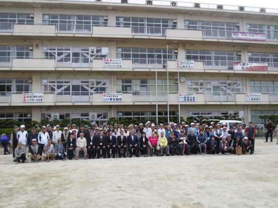 高州東小学校のグラウンドで校舎をバックに、三郷市長と131名の参加者が集まって並び記念撮影をしている写真