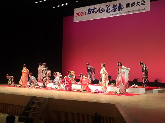 「日本の心と美の祭典関東大会」と書かれた横断幕下のステージで、着物を着ている女性たちが2列に並んでいるコンテストの様子を写した写真