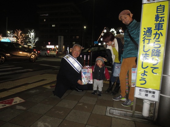 「自転車から降りて通行しましょう」の看板が立てられた歩道の一角で、1組の家族の子どもにキャンペーンのチラシを手渡している市長の写真
