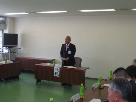 「会長」の貼り紙が貼られている席を立ち挨拶の言葉を述べる三郷市長と、席札とお茶のペットボトルが置かれた席に座り話を聞く関係団体のメンバーの写真