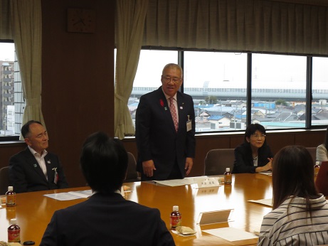 席を立ち鈴木奏さんの発表の感想を述べる三郷市長と、席札とペットボトルのお茶が置かれている席に座り話を聞く関係者の写真