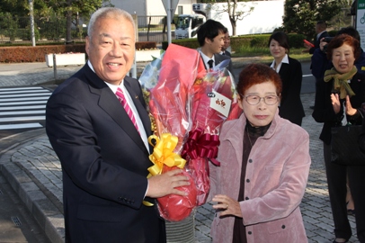 薄ピンク色のジャケットを着た女性から花束を頂いた笑顔の市長の写真