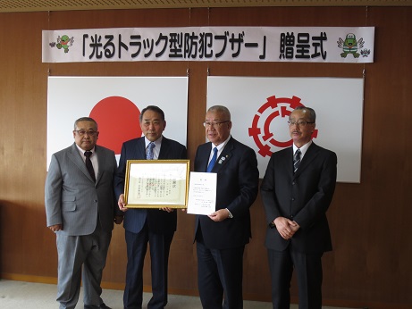 「光トラック型ブザー」贈呈式にて、三郷市長が関田吉川支部長と感謝状を手に持った埼玉県トラック協会吉川支部の関係者とともに記念撮影をしている写真