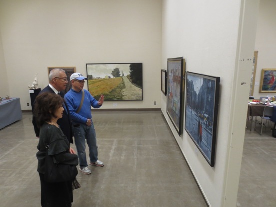 多数の絵画が展示されている部屋で、市長と2名のかたが一つの作品の前に立って鑑賞している写真