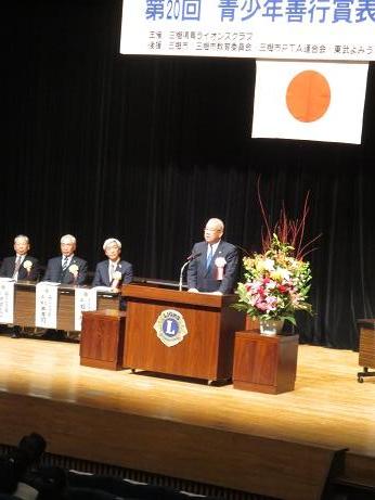 「第20回青少年善行賞表彰状授与式」と書かれた横断幕下の演壇で挨拶を行っている市長の写真