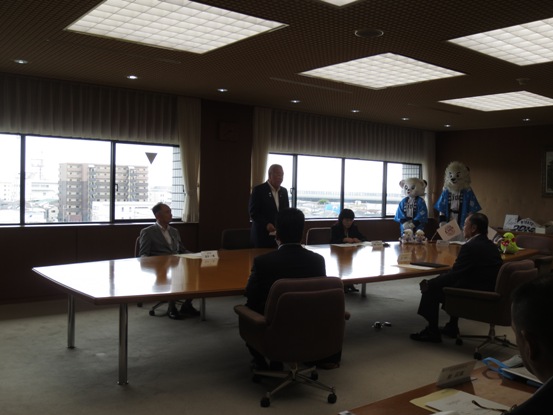 部屋に大きなテーブルが設置され、椅子に座っている関係者と立っている市長、部屋の奥にはライオンズのキャラクターの2人が立っている写真