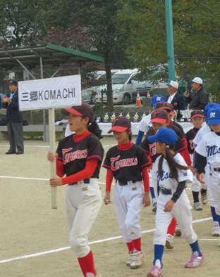 先頭の選手が「三郷KOMACHI」と書かれたプラカードを持ち、続いて選手たちが行進している様子の写真