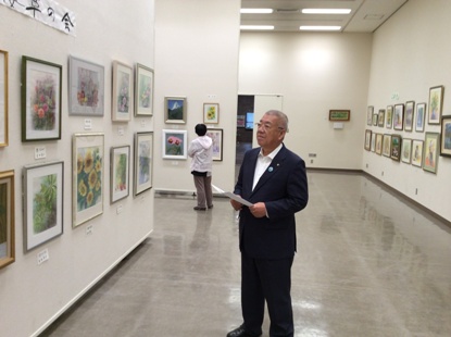壁に沢山の絵画作品が展示された展示室内で作品を鑑賞している市長の写真