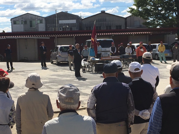 屋外の敷地で、大会参加者たちの前に立ってマイクを手に話をしている市長の写真