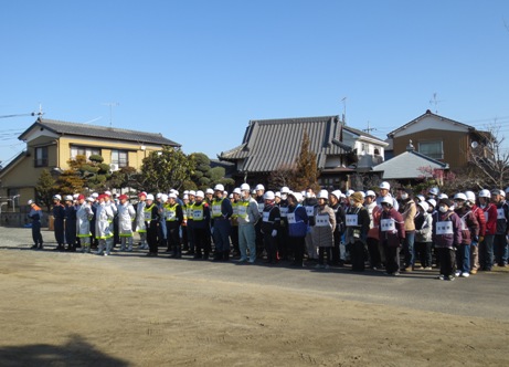 東光院の瓦屋根の建物を背に、広場に並んで立つ、ヘルメットとゼッケンをつけたたくさんの訓練参加者たちの写真