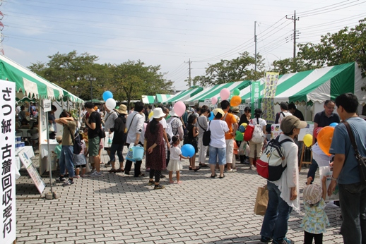 屋外に並んで設置された緑色と白色のテントに大勢の家族連れのお客さんが並んでいる写真