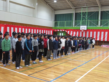 紅白幕が掛けられた体育館で、整列した子どもたちが合唱を披露している写真