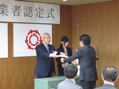 「認定農業者認定式」と書かれた横幕が壁に貼られた室内で向かい合って立っている男性に市長が認定書を授与している様子の写真